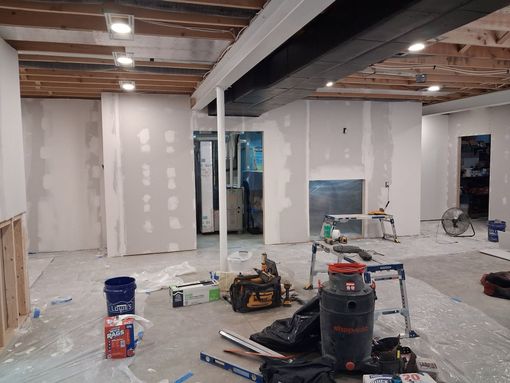 Partially renovated basement with drywall, exposed beams, tools, and plastic sheeting on the floor