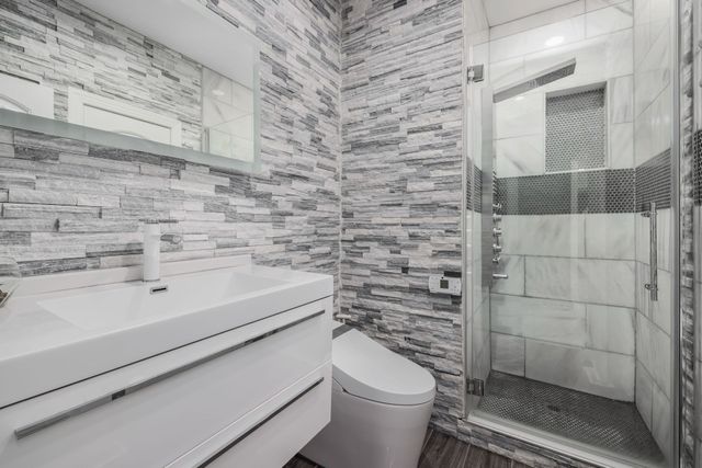Modern bathroom with white vanity, toilet, and glass shower, accented by gray brick-pattern tile walls.