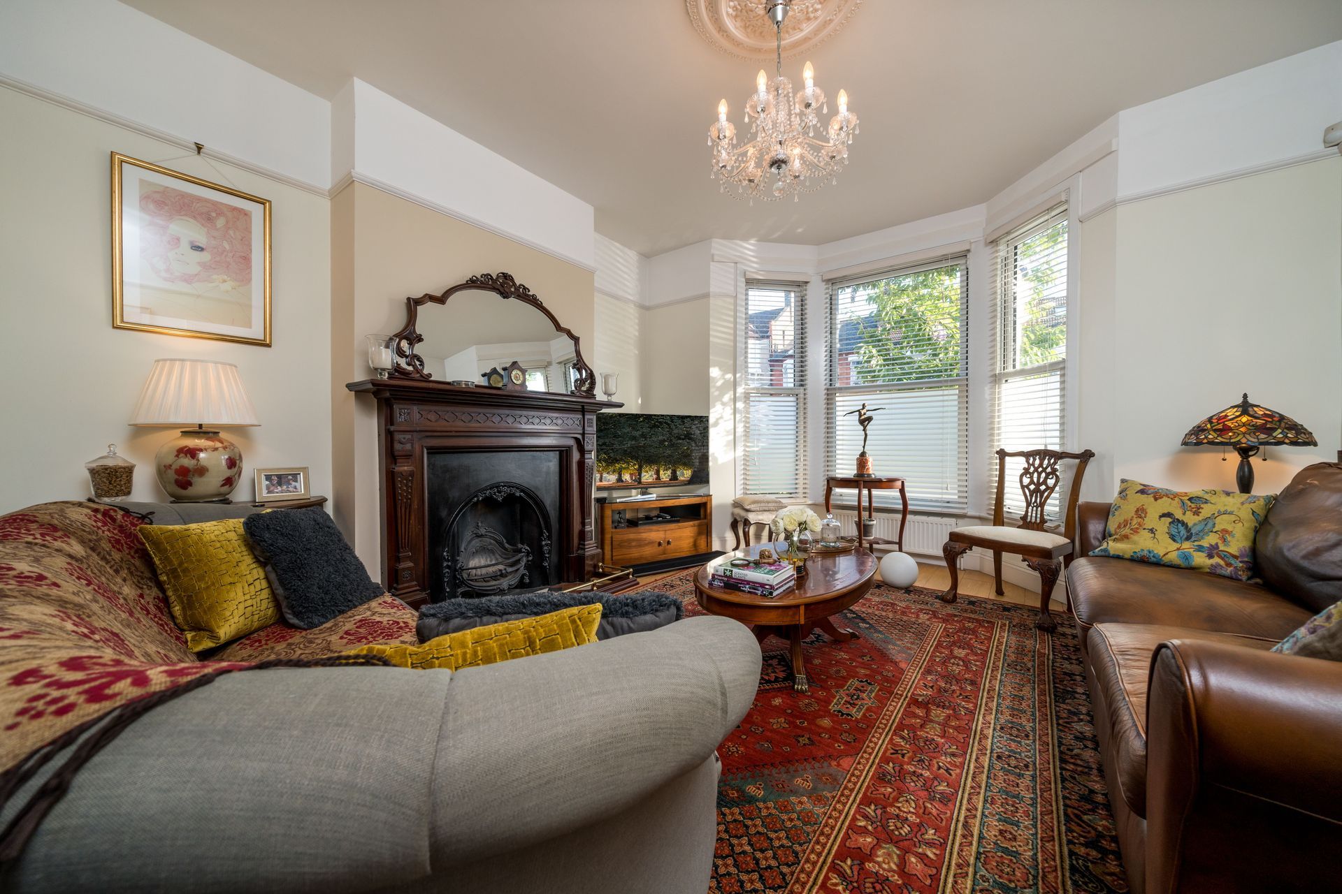 Elegant living room with fireplace, chandelier, patterned rug, and upholstered sofas by a bay window.