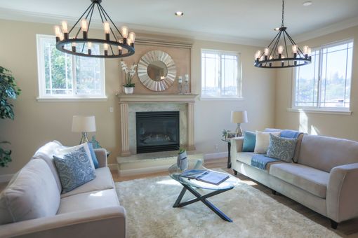 Bright living room with two sofas, fireplace, chandelier lights, and a glass coffee table