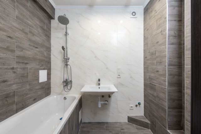 Small bathroom with white marble walls, bathtub, wall-mounted sink, and shower fixture on the left.