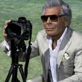 Un homme en costume tient un appareil photo sur un trépied