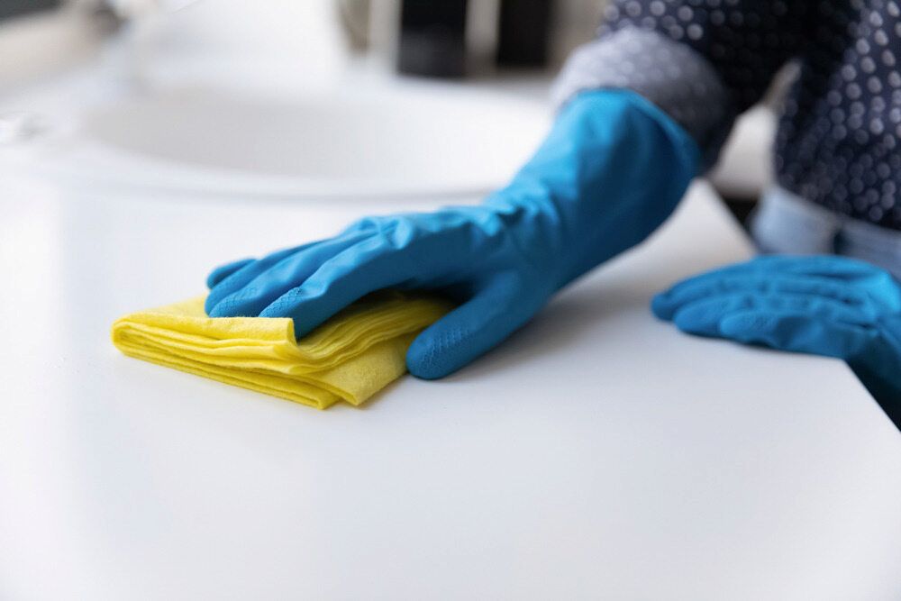 A Person Wearing Blue Gloves Is Cleaning A Counter With A Yellow Cloth — Proud Cleaning Canberra in Red Hill, ACT