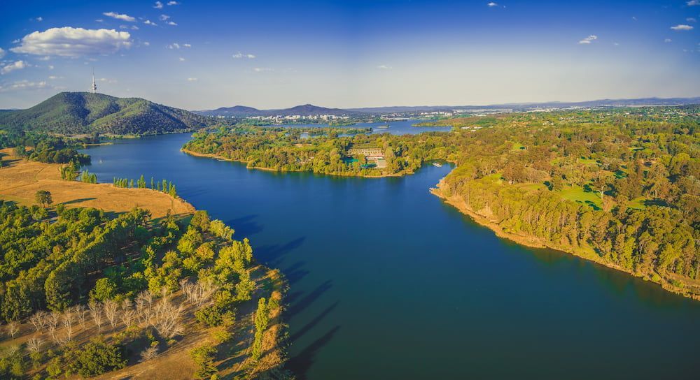 An Aerial View Of A Lake Surrounded By Trees And Mountains — Proud Cleaning Canberra in Weston, ACT