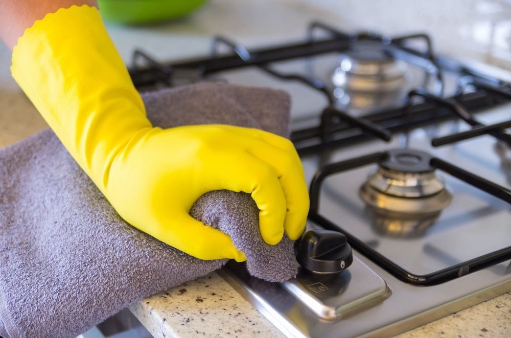 A Person Wearing Yellow Gloves Is Cleaning A Stove Top With A Towel — Proud Cleaning Canberra in Weston, ACT