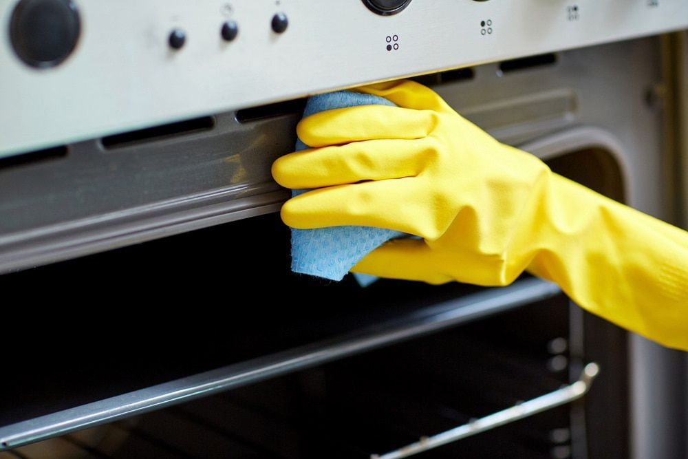 A Person Wearing Yellow Gloves Is Cleaning An Oven With A Sponge — Proud Cleaning Canberra in Red Hill, ACT