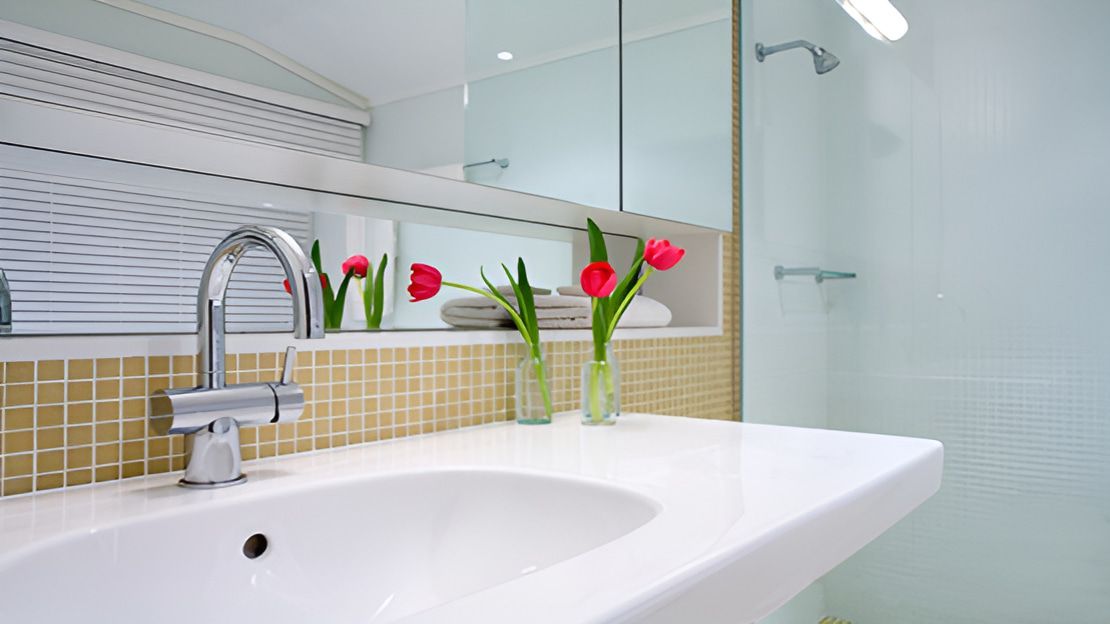 A Bathroom With a Sink, Mirror and Vase of Flowers — Proud Cleaning Canberra in Amaroo, ACT