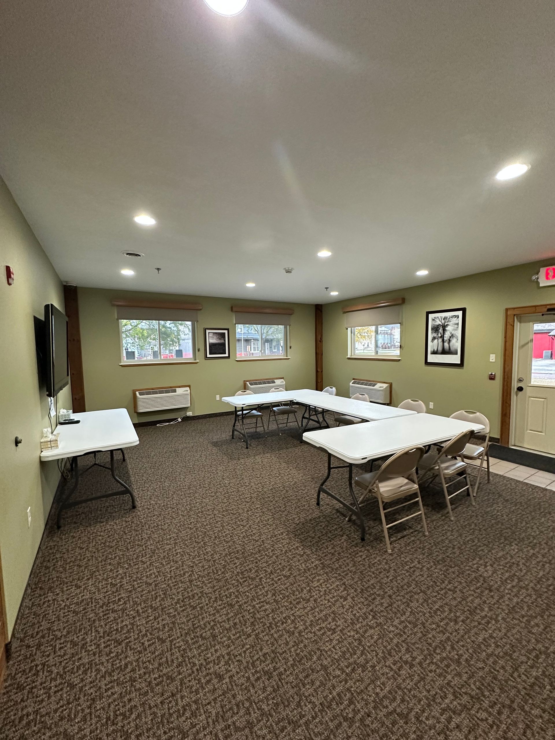 Conference room with folding tables arranged in a horseshoe shape, brown carpet, and small artwork on walls.