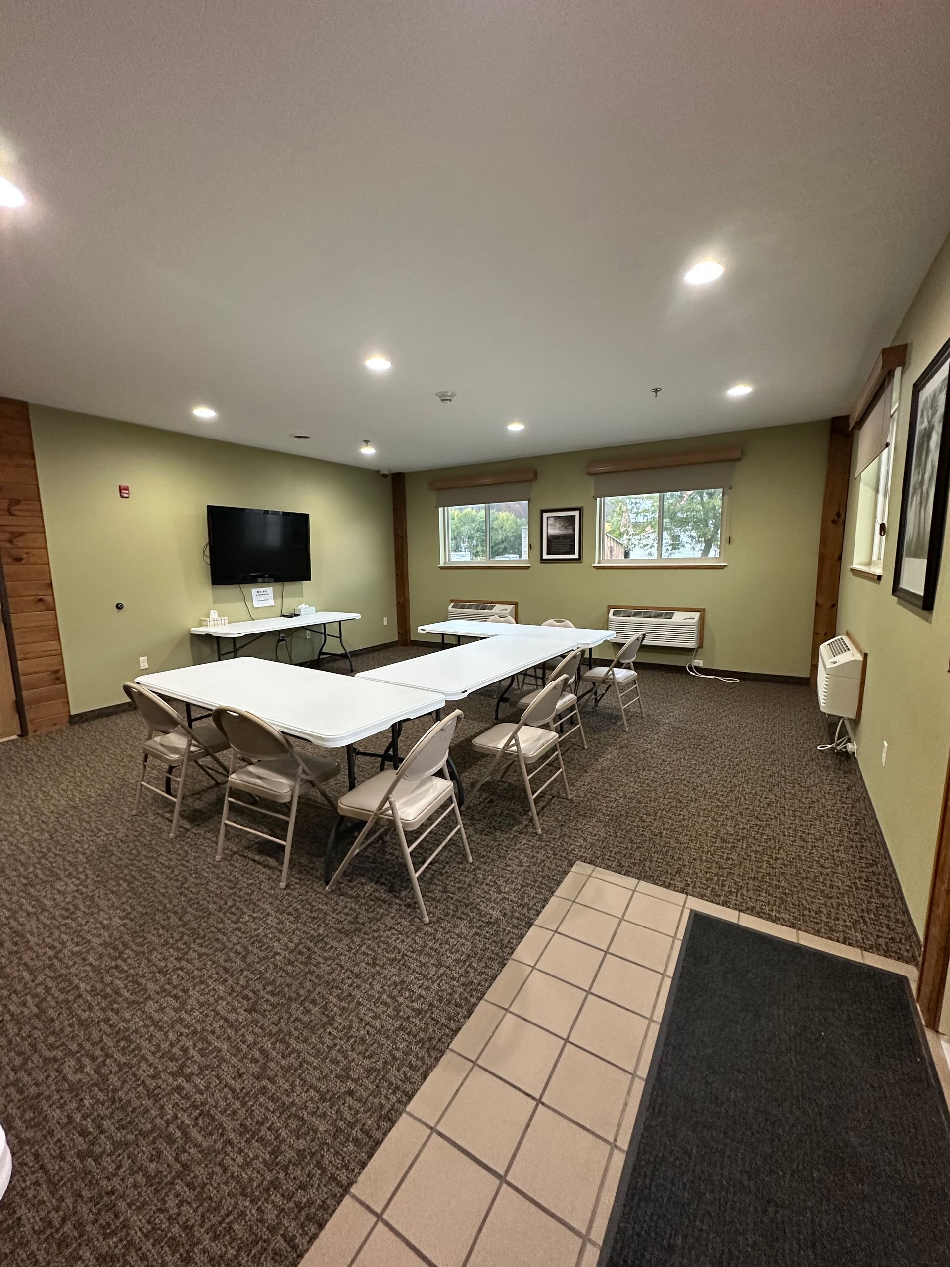 Conference room with U-shaped table and chairs, TV, windows, and neutral carpet.