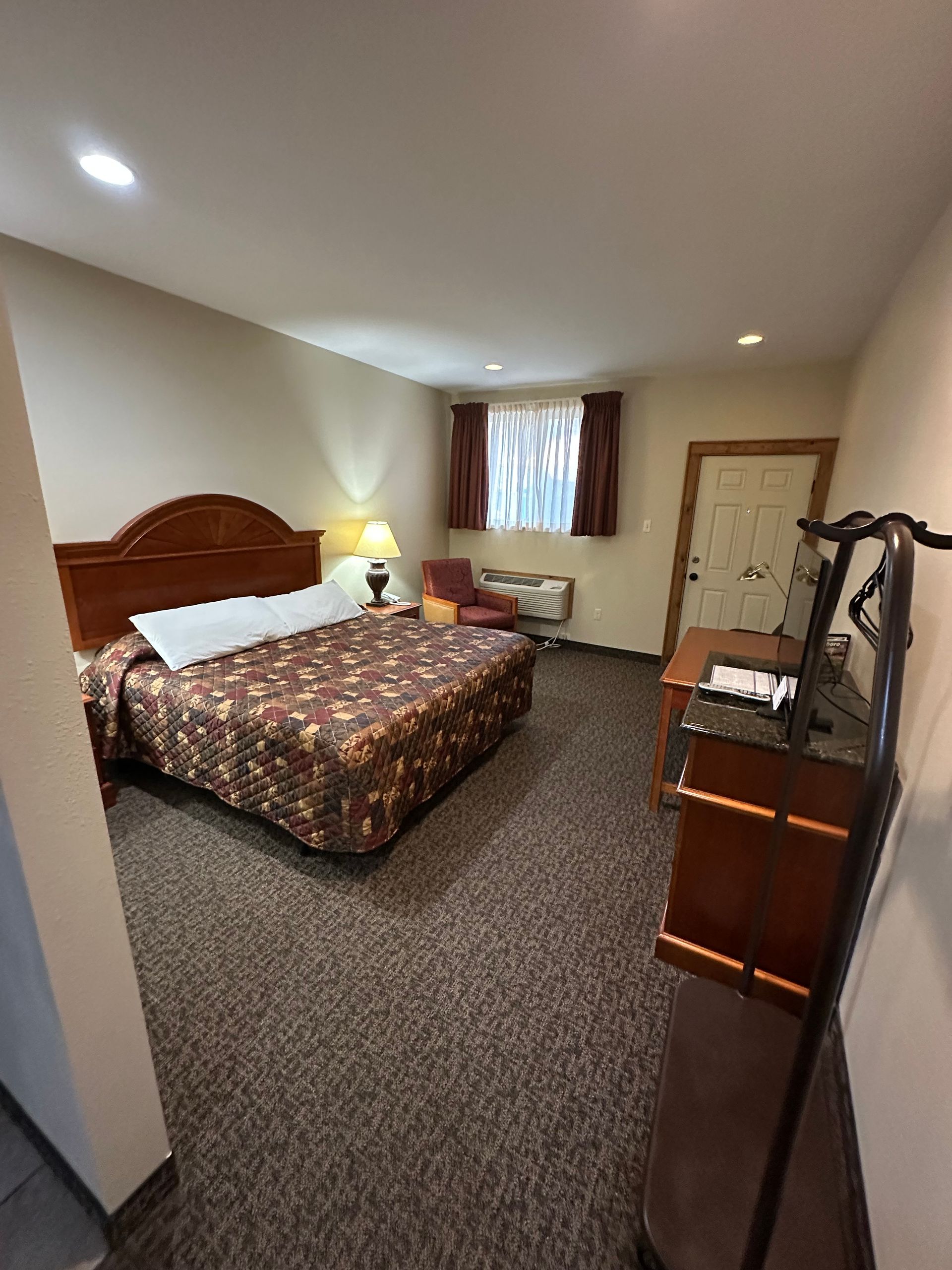 Bedroom with bed, chair, and dresser. Brown carpet, walls, and patterned bedspread.