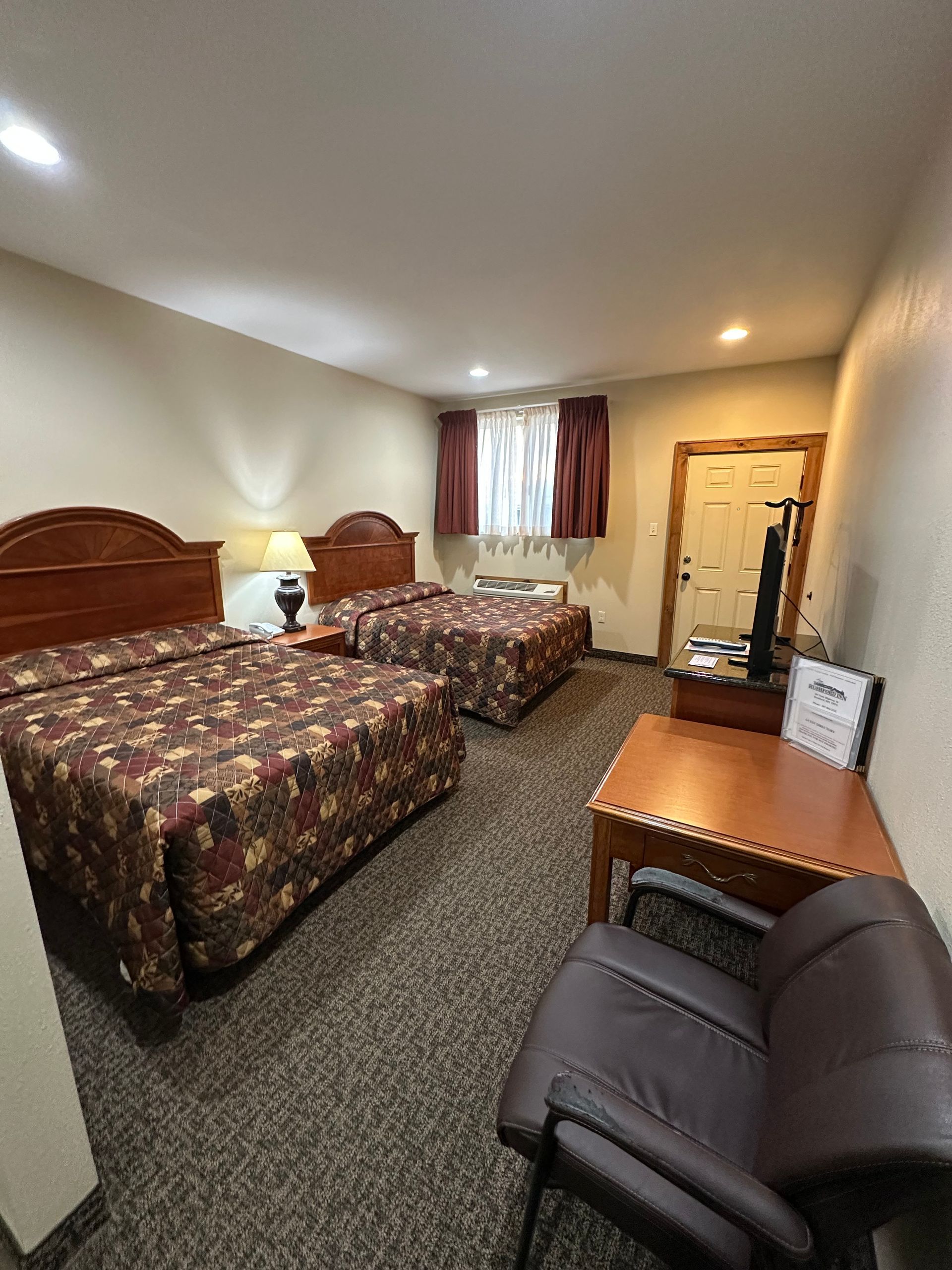 Hotel room with two double beds, brown floral bedspreads, brown carpet, desk, and chair.