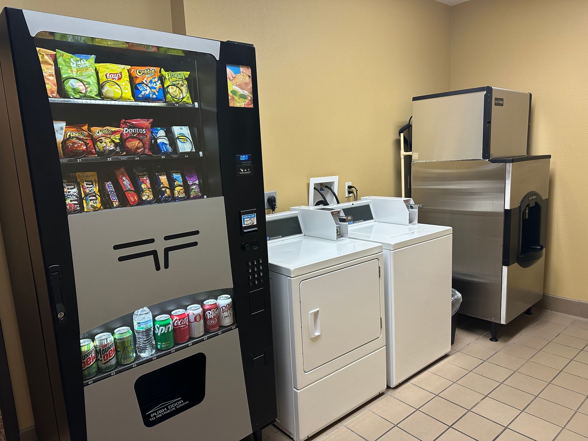 Vending machine, laundry machines in a room with tiled floor and beige walls.