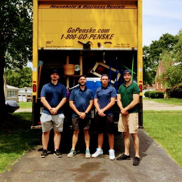 Five men stand in front of a yellow Penske truck on a driveway, posing for a photo.