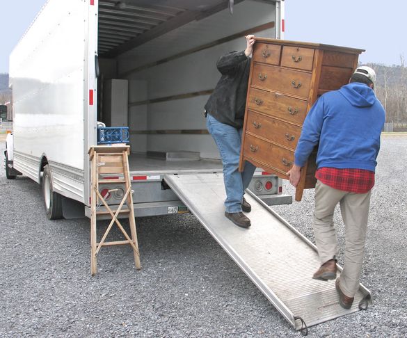 Two people carrying a wooden dresser up a ramp into a moving truck