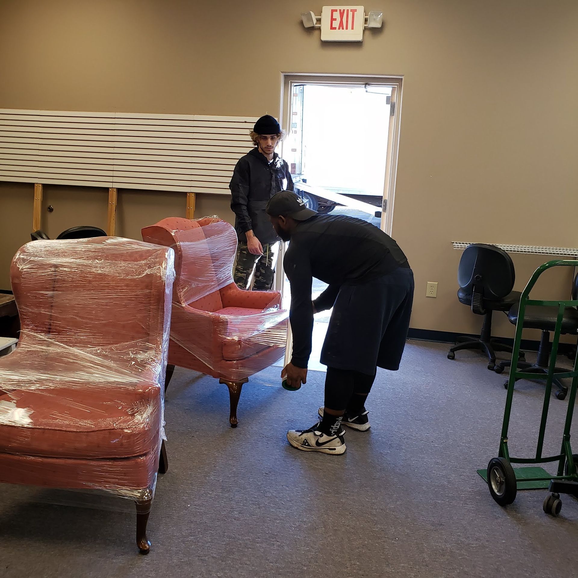 Two workers moving red upholstered chairs in a room near an open exit door