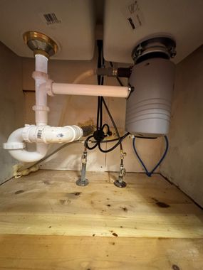 Plumber in blue cap tightening a pipe valve beside a water filtration system in a utility room