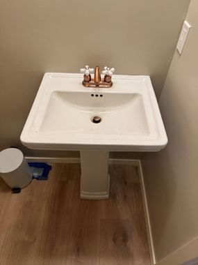 Plumber tightening a bathroom sink drain pipe with pliers under the sink