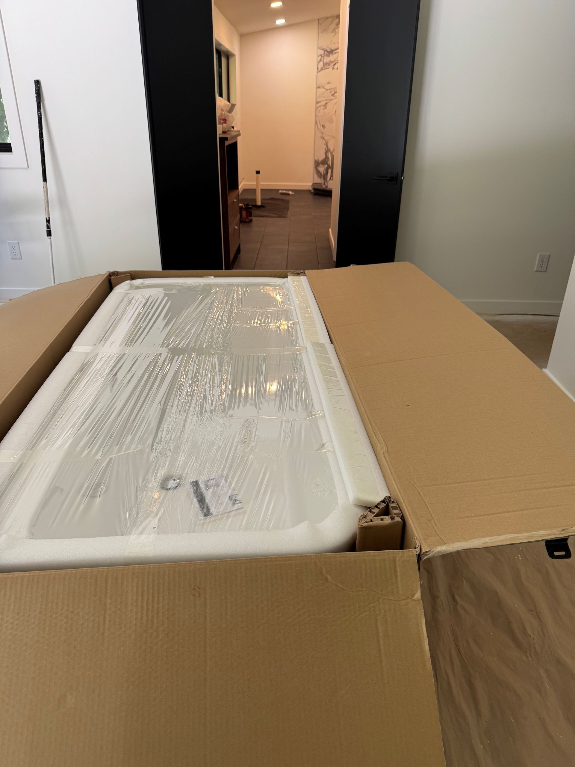 Open cardboard box with a white bathtub inside, in a hallway doorway.