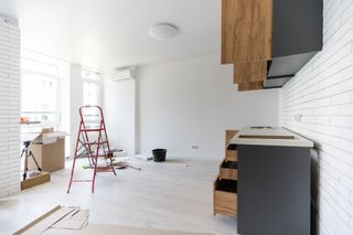 Unfinished kitchen with red step ladder, white walls, gray cabinets, and wood countertops under renovation