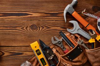 Assorted hand tools on a wooden workbench, including hammers, wrenches, a level, and a saw.
