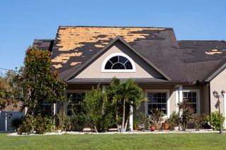House with damaged roof and missing shingles in a sunny suburban yard