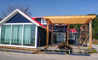 House under construction with a wooden porch frame and a blue façade with large windows