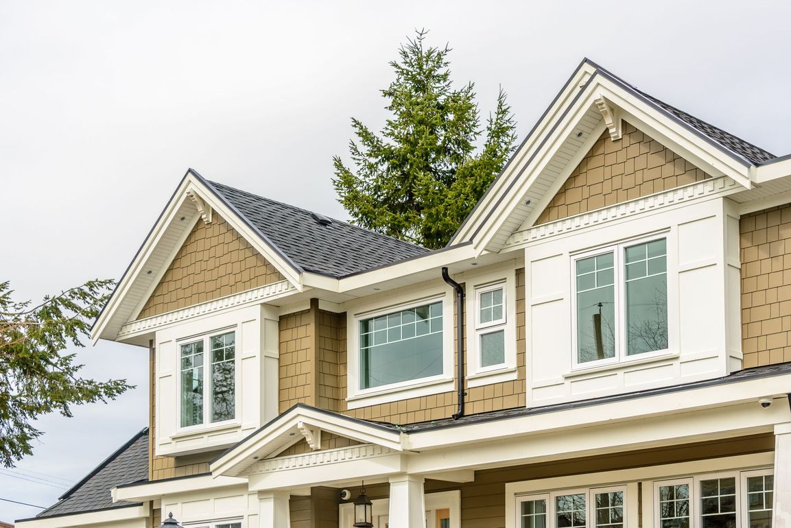 Two-story suburban house with cream siding, dark gray roof, and dormer windows under a cloudy sky