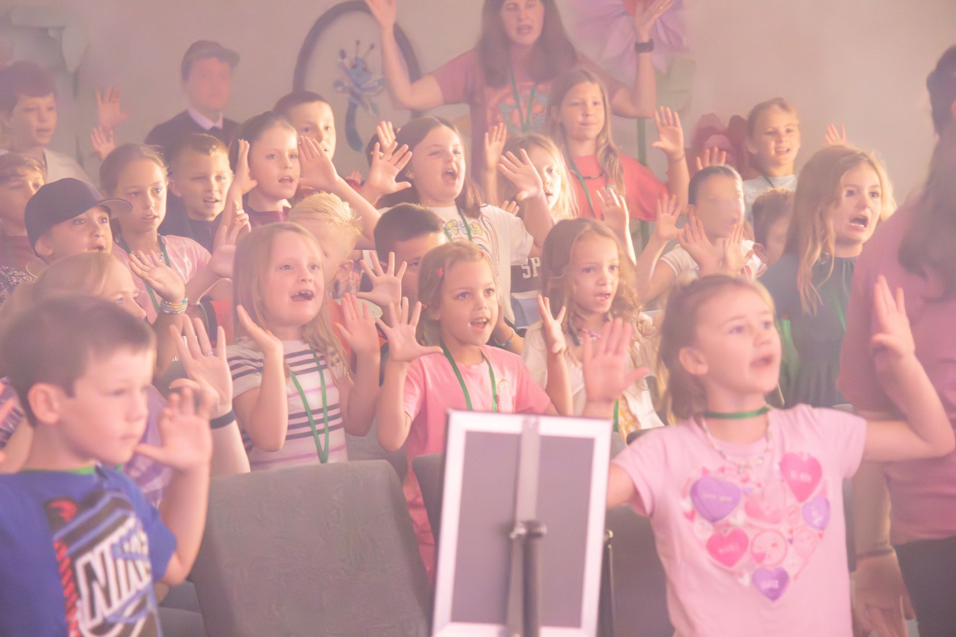 Audience of children clapping enthusiastically in a bright, indoor church sanctuary.