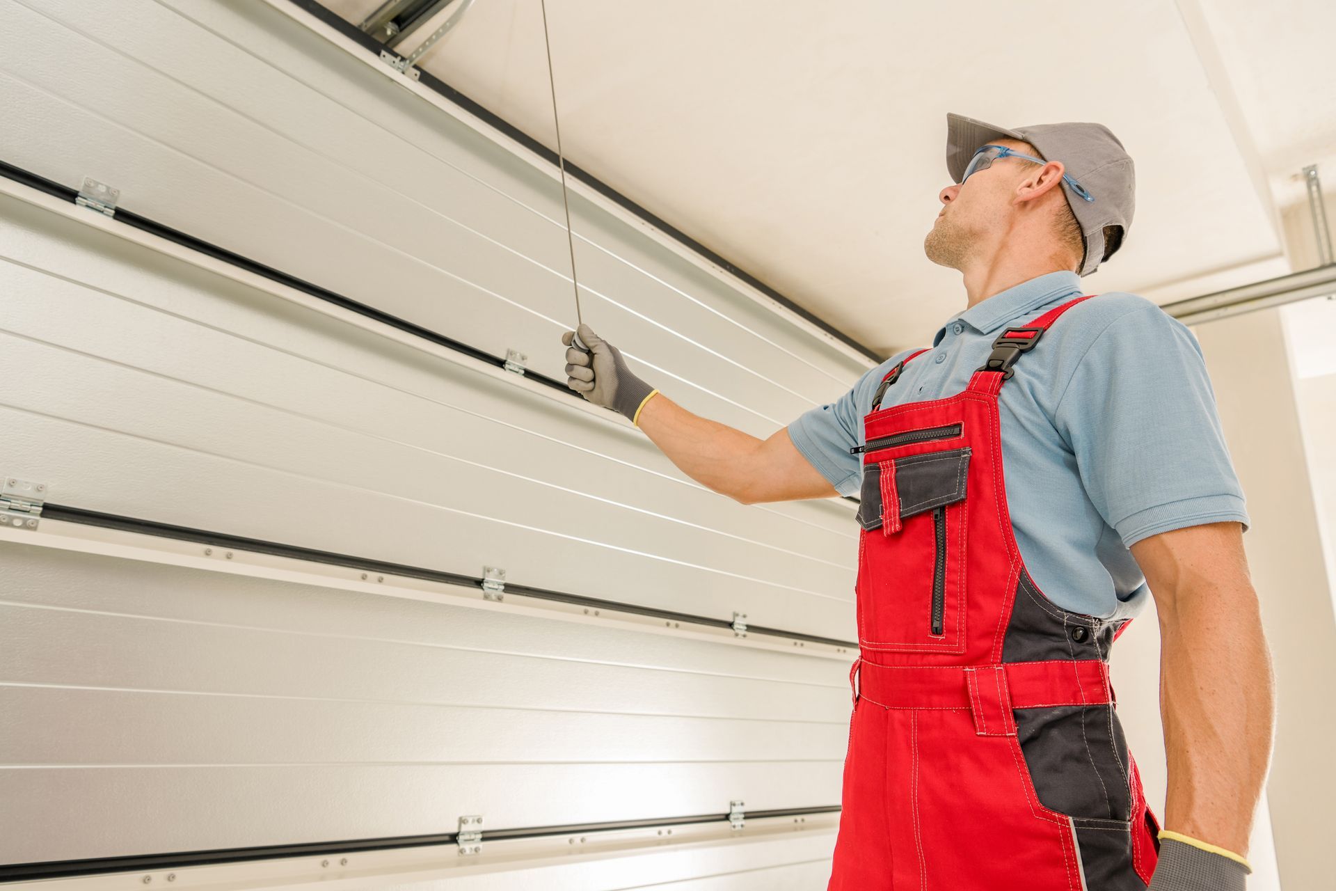 A man in red overalls is working on a garage door.