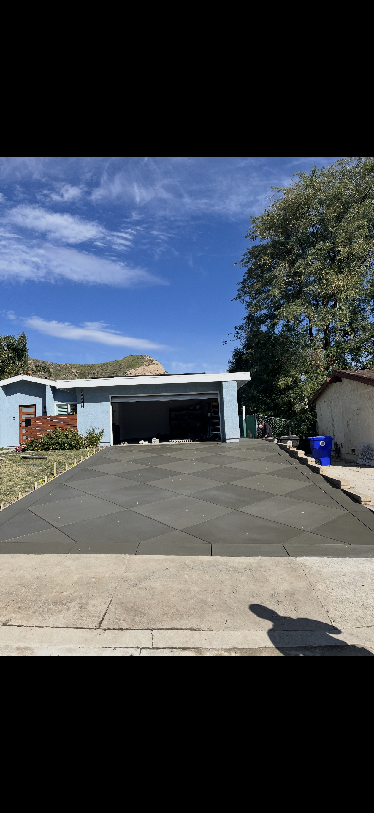 A house with a newly paved driveway on a sunny day. The garage door is open.