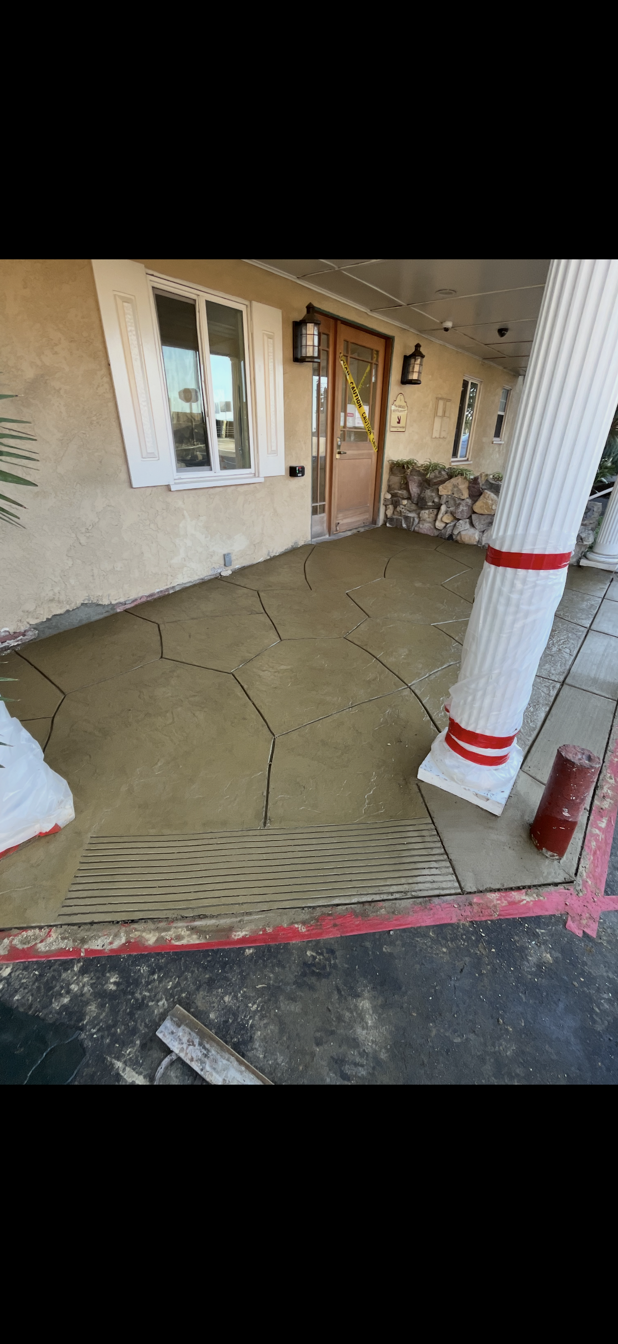 A building's concrete porch with decorative lines and red trim, leading to a wooden door and window.