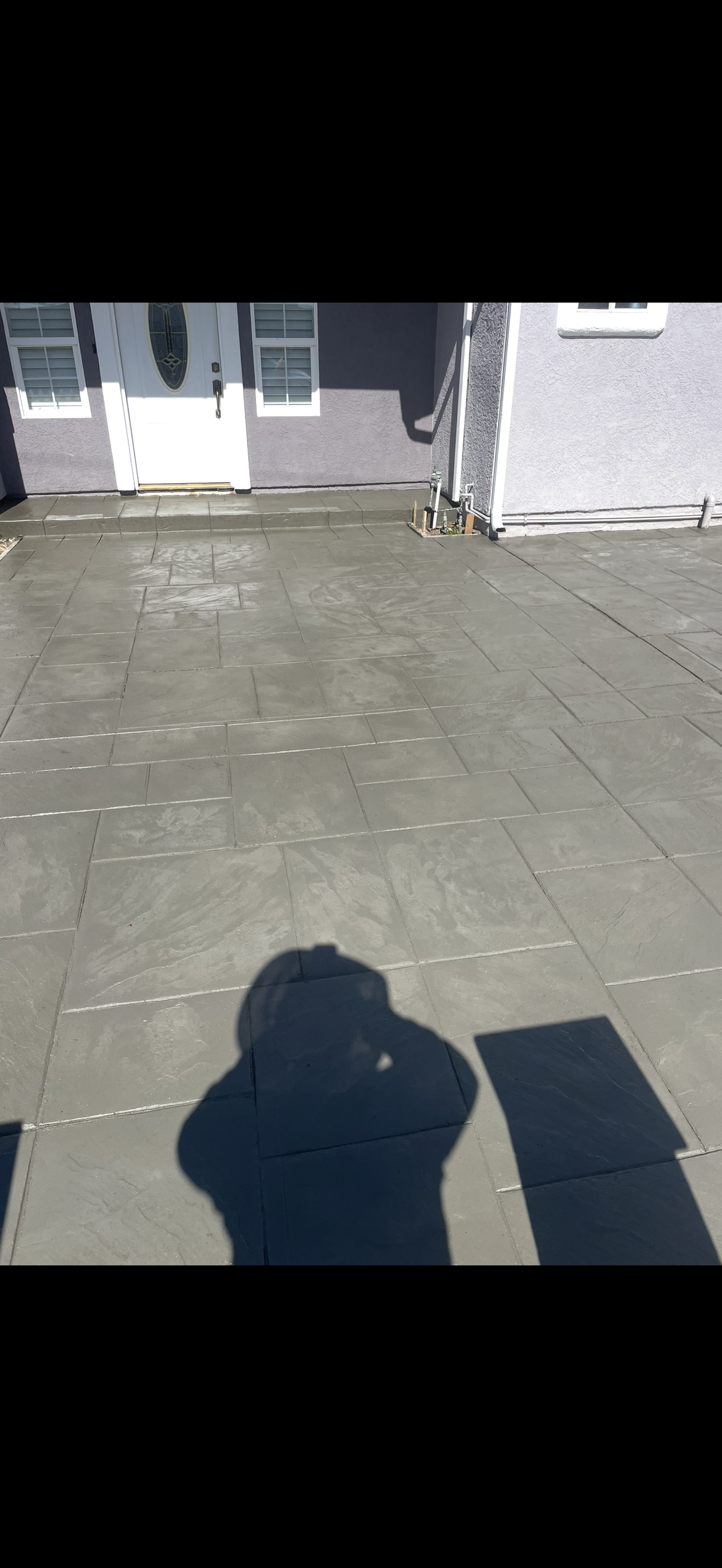 Shadow of a person taking a photo on a paved area, a building in the background.