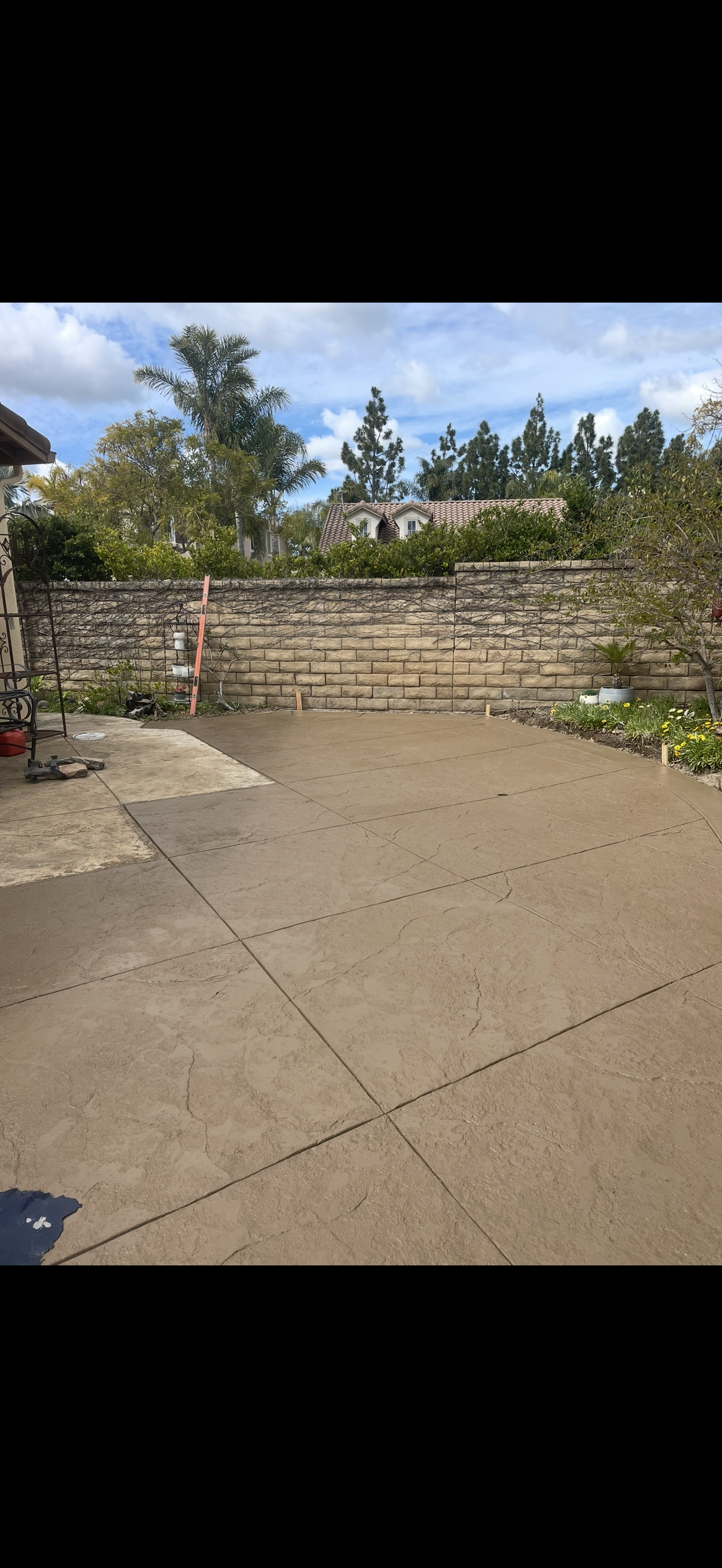 A concrete patio with a stone wall in the background, trees, and a cloudy sky.
