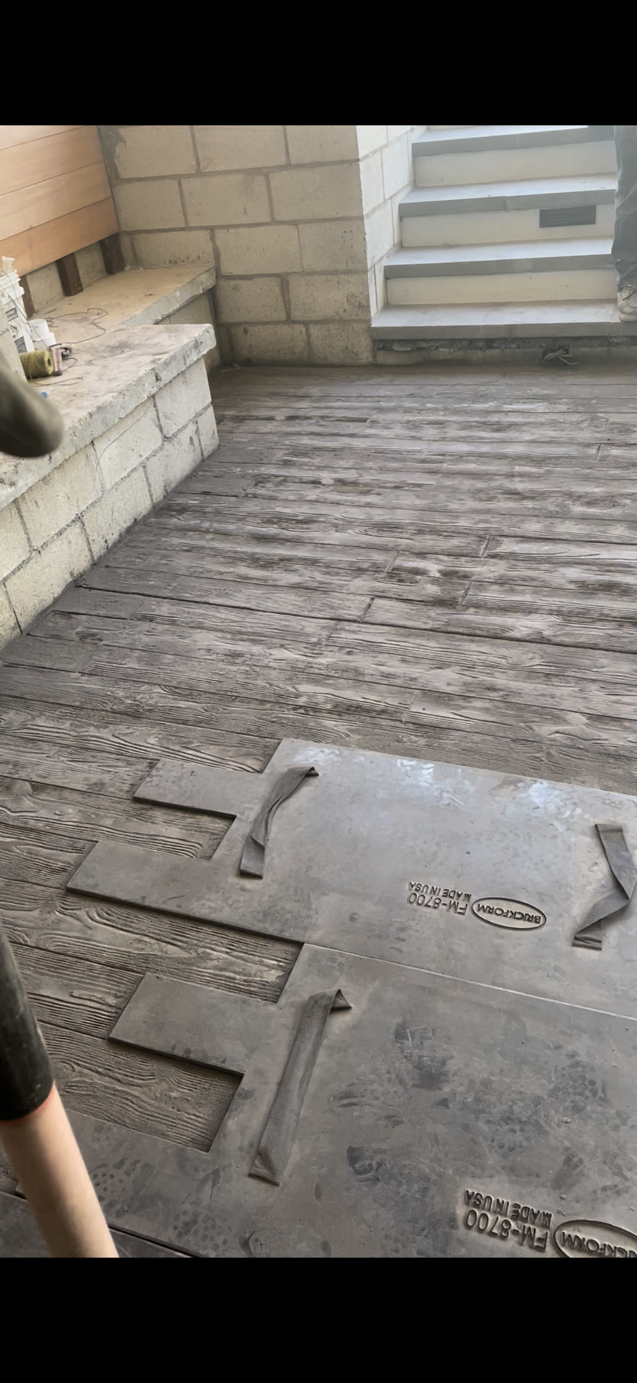 Person working on a concrete patio, using a textured stencil to create a pattern.