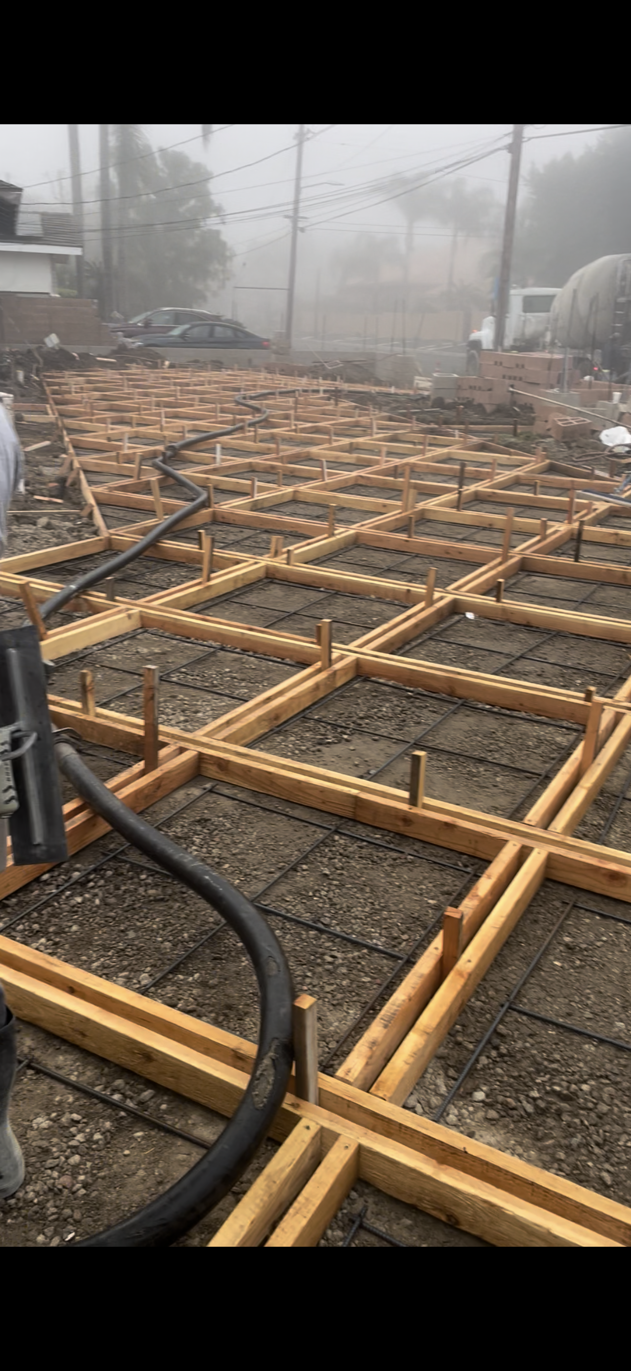 Construction site with wooden forms and rebar grids, ready for concrete pouring. Overcast day.