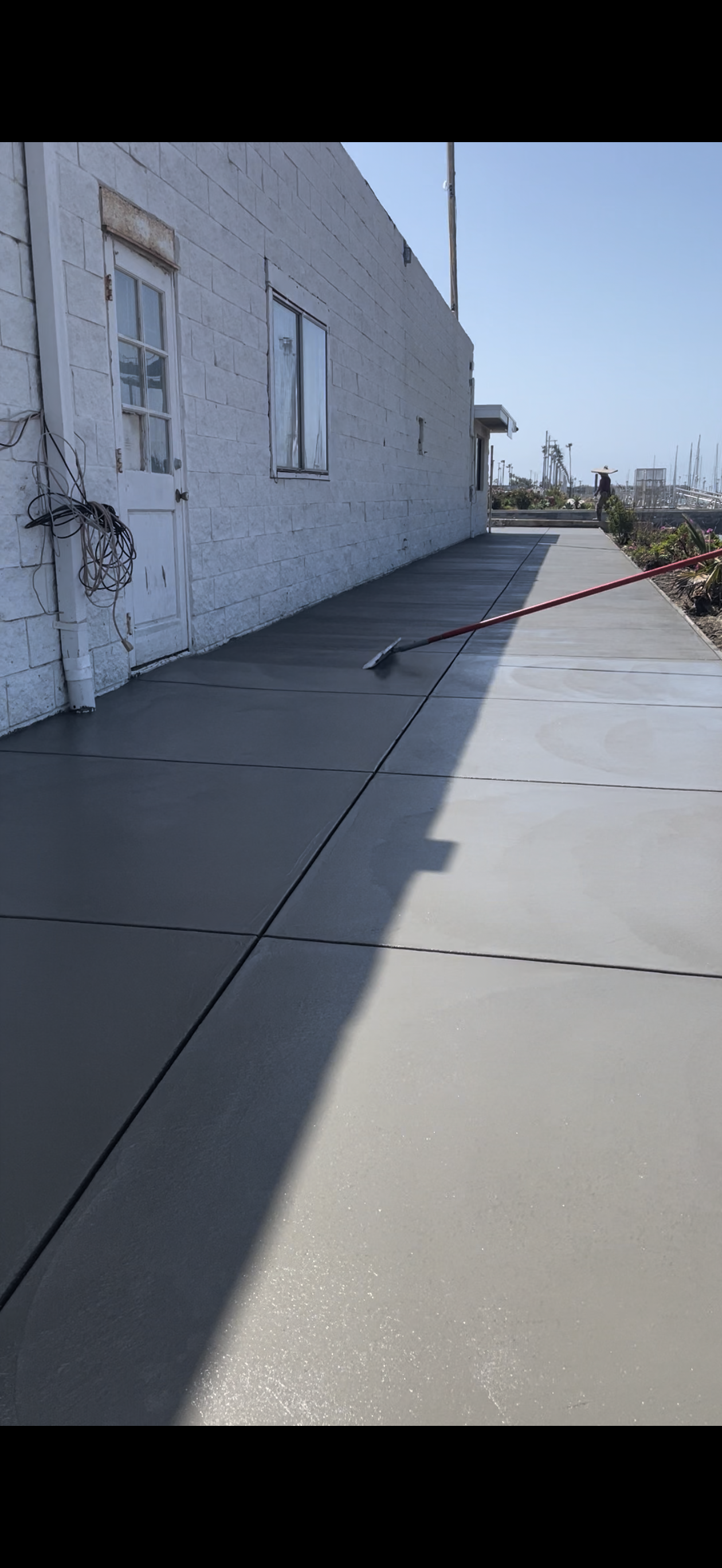 Freshly poured concrete sidewalk next to a white brick building on a sunny day.