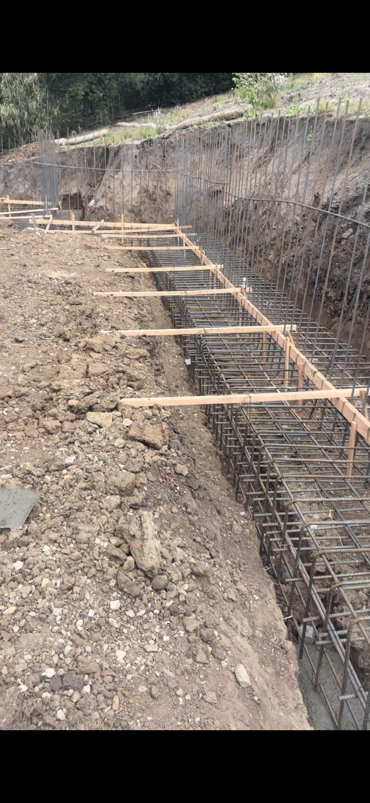 Construction site with a trench dug. Rebar framework and wooden supports are visible. Earth backdrop.