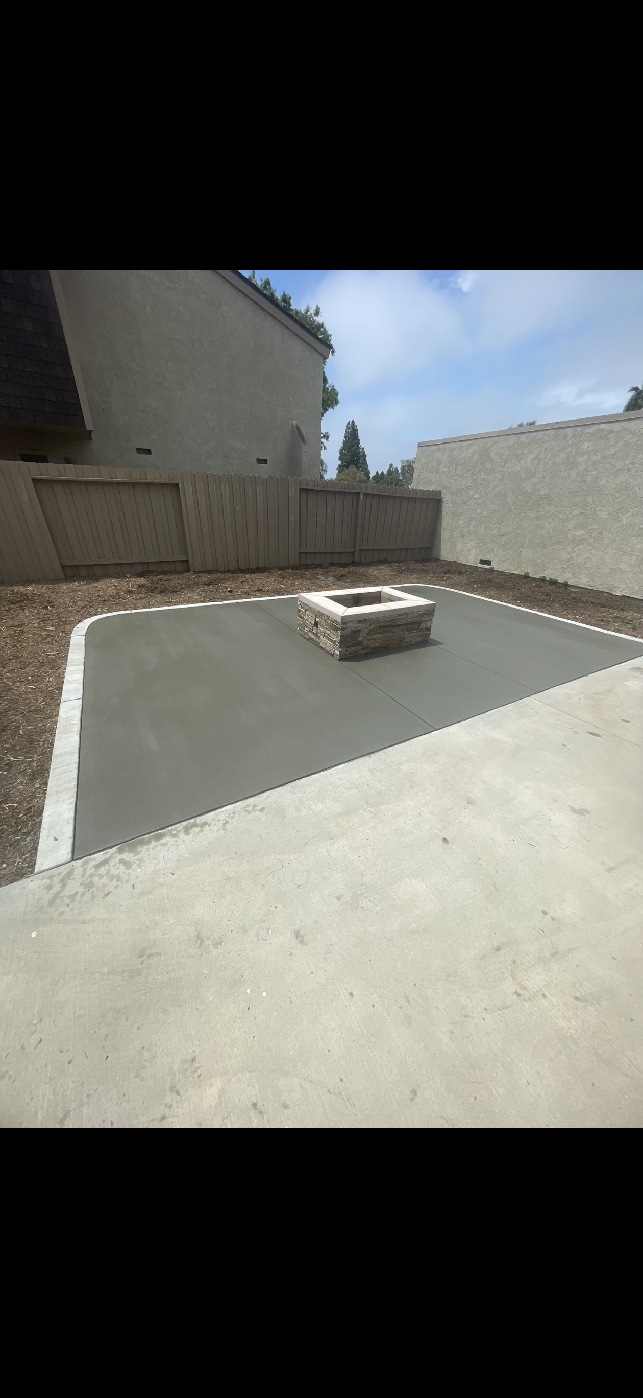 Backyard patio with a fire pit surrounded by a concrete surface and gravel.