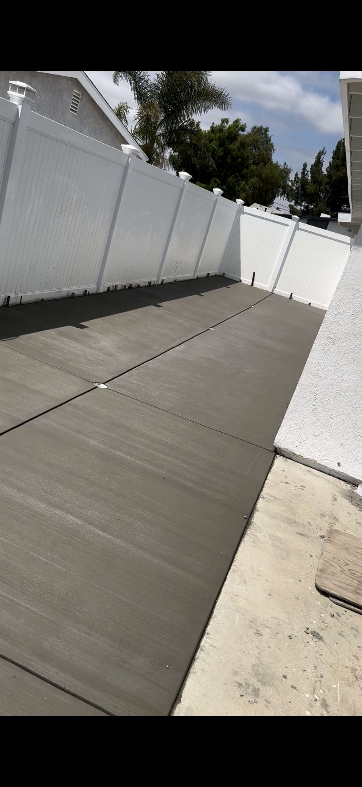 Freshly poured concrete patio surrounded by white fences under a blue sky.