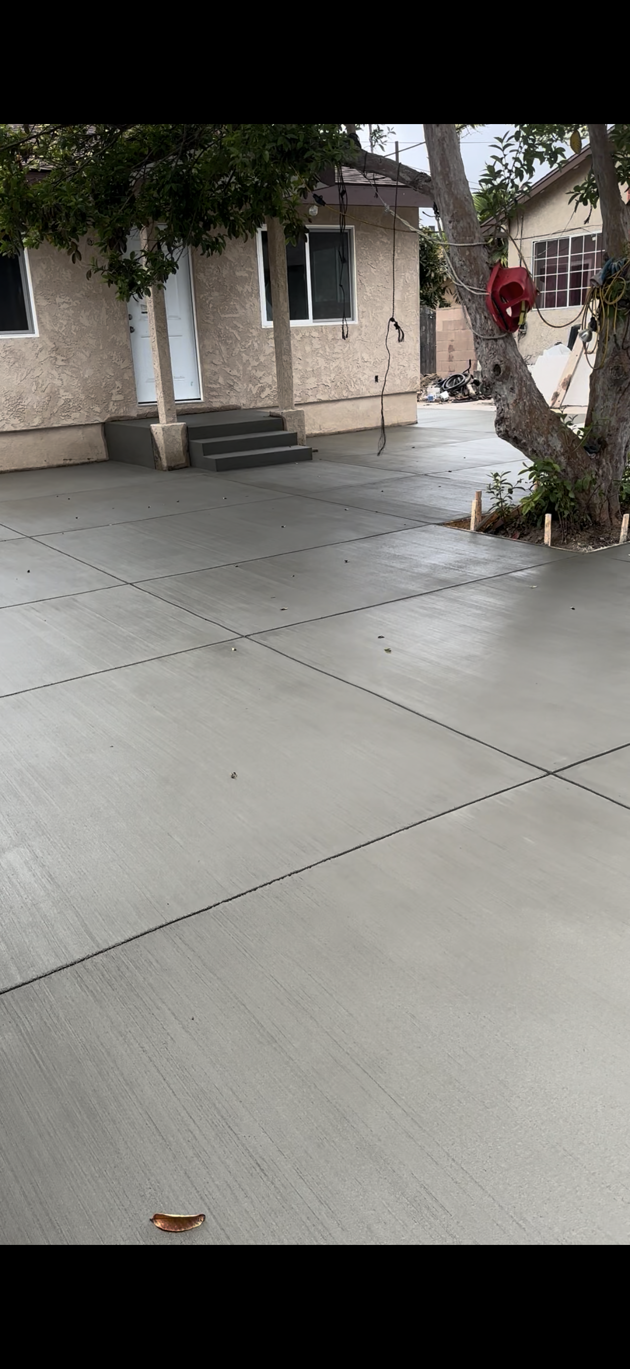 Newly poured concrete driveway with a house in the background and a tree on the right side.