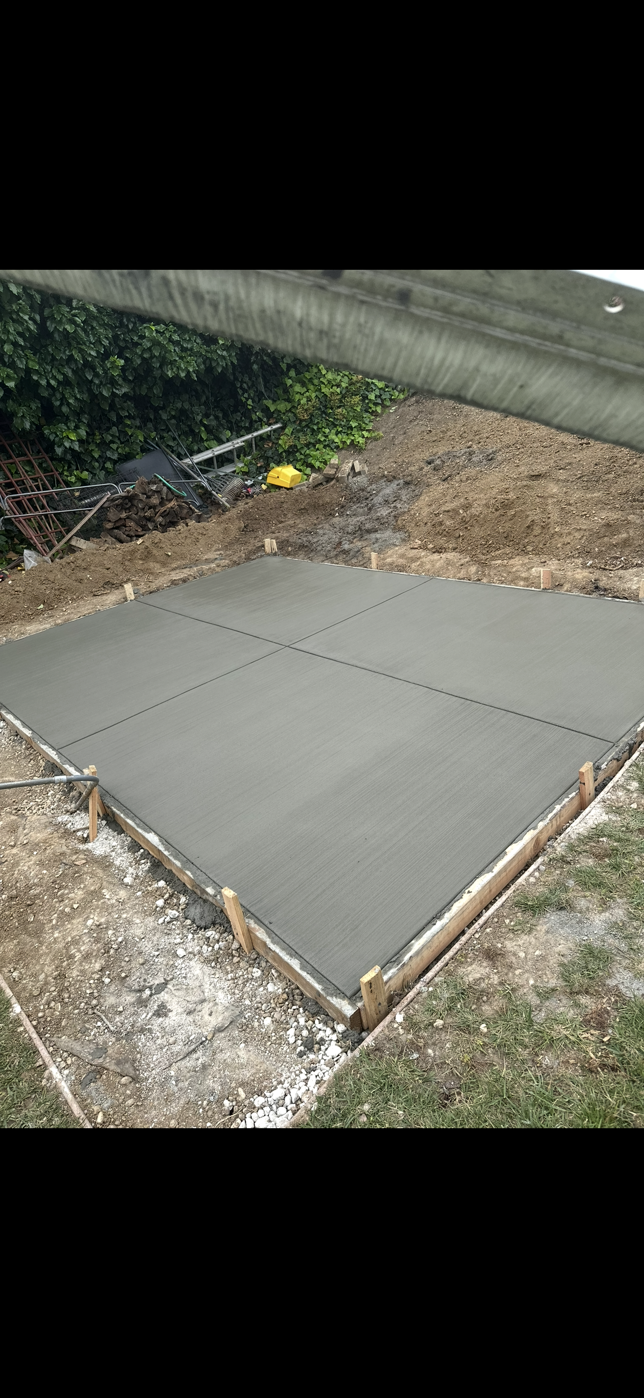 A freshly poured concrete pad framed by wooden boards, set in a yard with grass and dirt.
