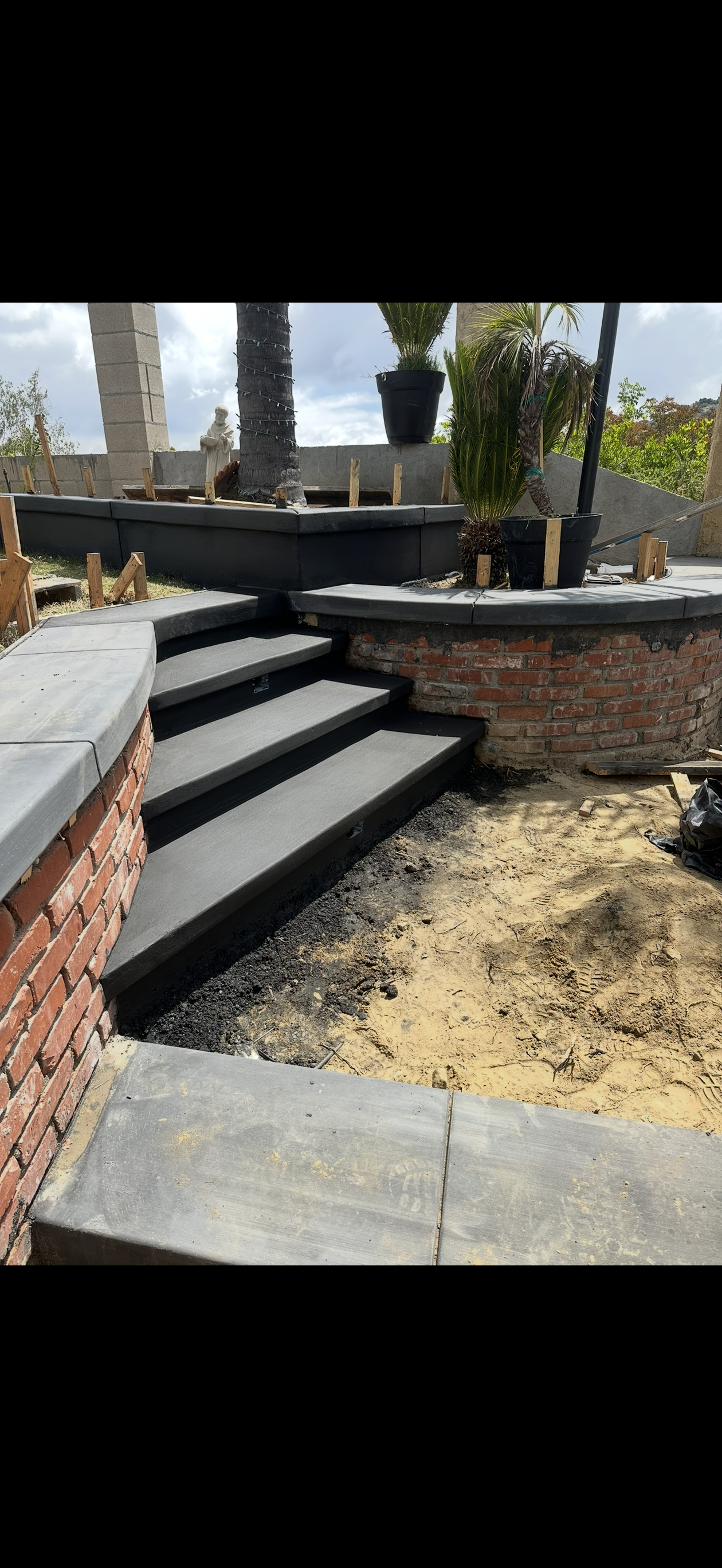 Stone steps leading up, constructed next to a brick wall. The ground in front of the steps is sand.