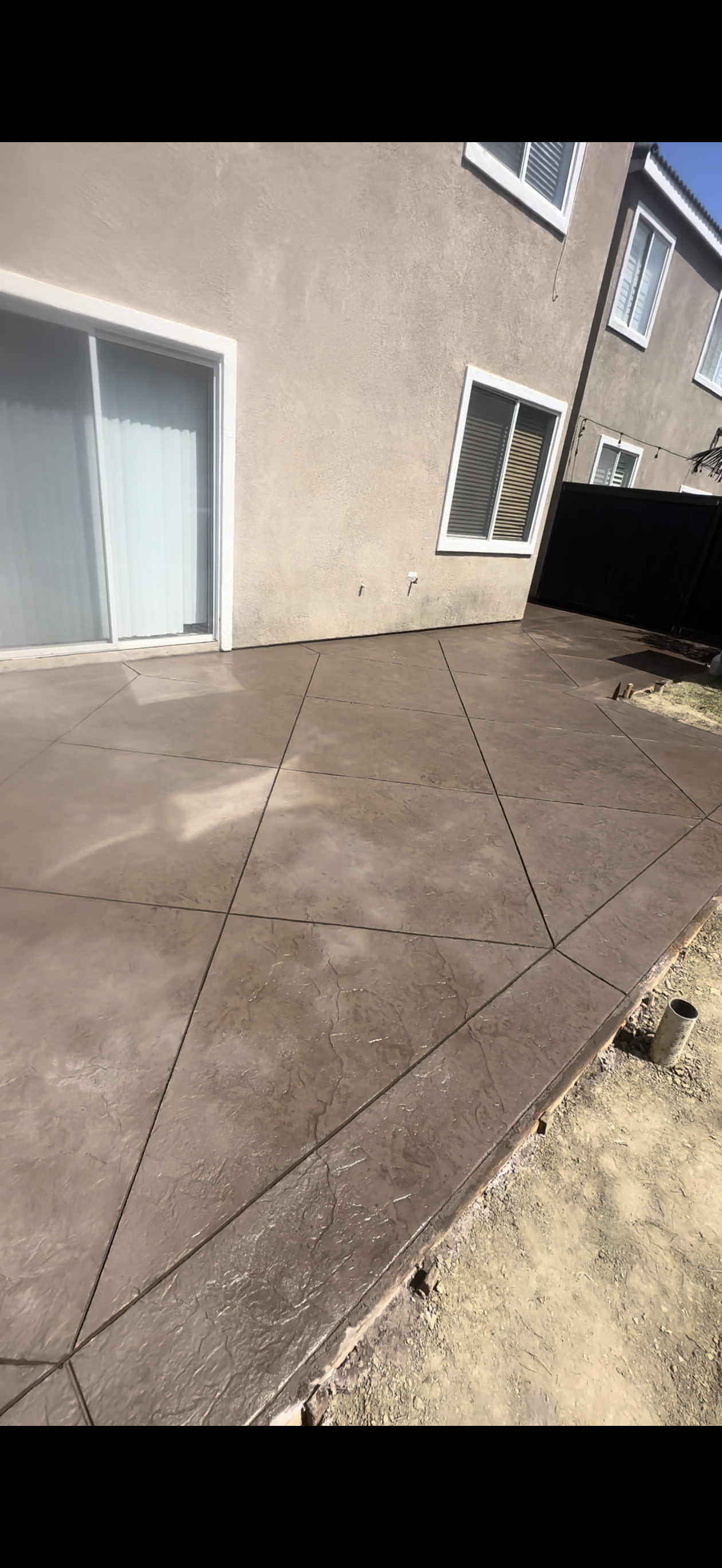 Concrete patio with dashed lines, next to a beige house, with a sliding glass door and windows.