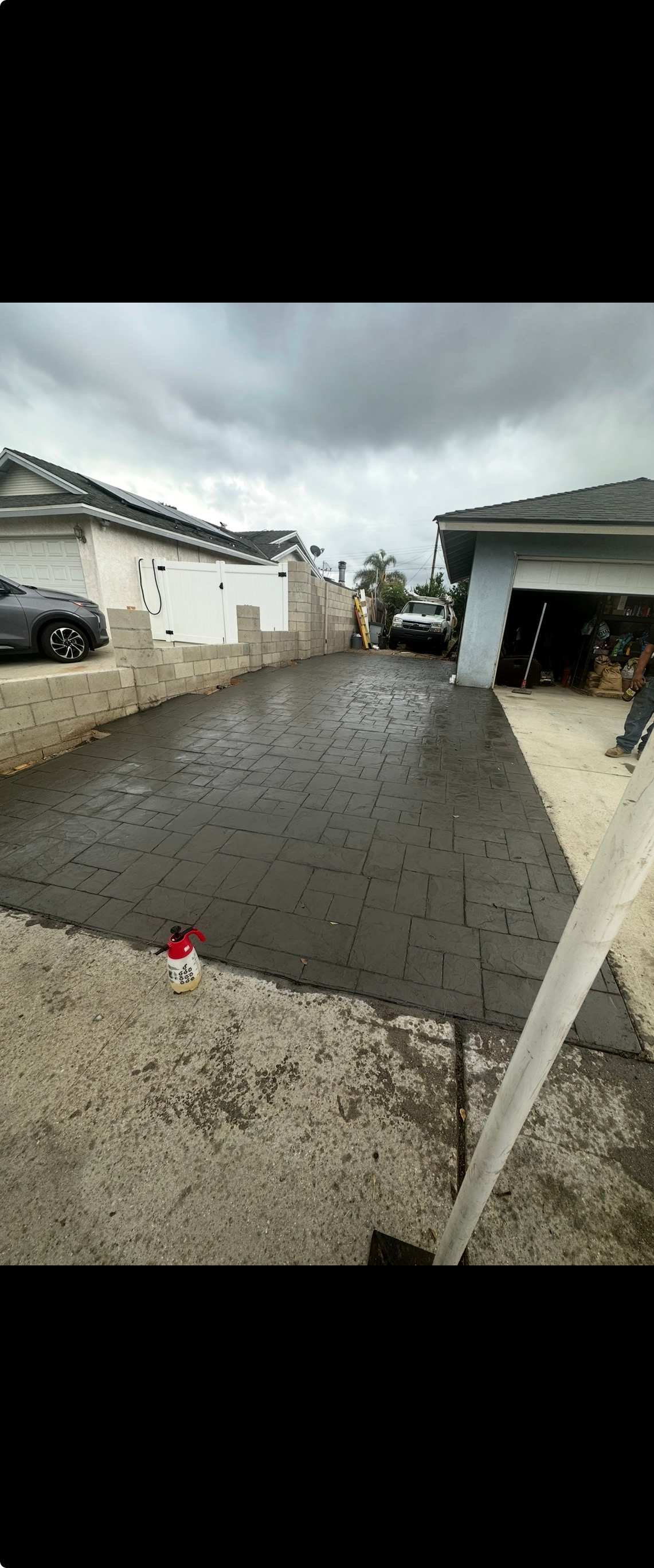Newly paved driveway between two houses, overcast sky.