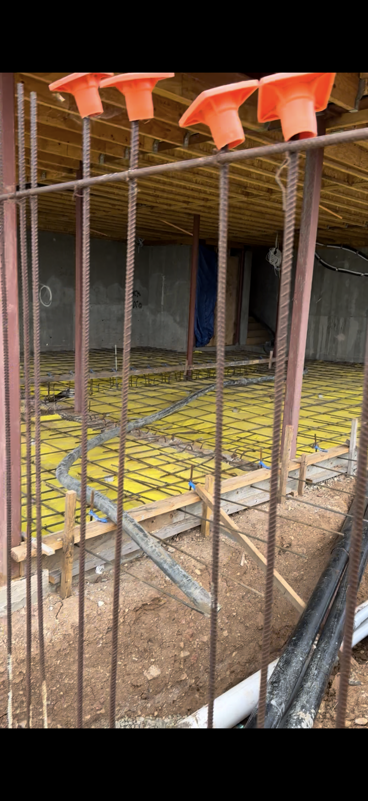 Construction site with exposed rebar, orange safety caps, and yellow insulation.