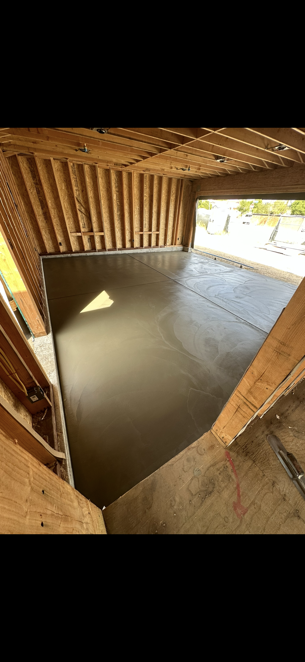 Interior view of a building under construction, featuring a concrete floor and wooden framing.