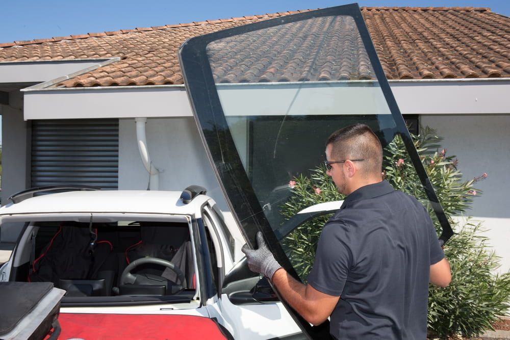 A Man Is Installing a Windshield on A Car in Front of A House — A1 Windscreens in Taminda, NSW