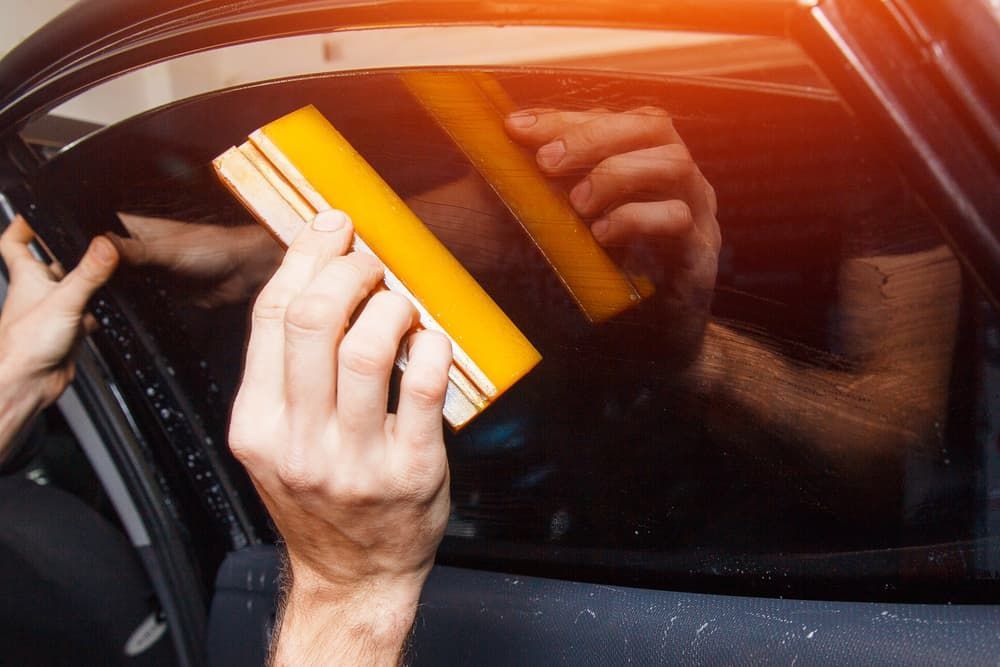 A Person Is Applying Tinted Window Film to A Car Window — A1 Windscreens in Gunnedah, NSW
