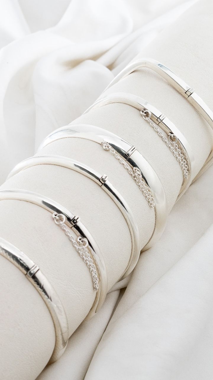 Pulseras apiladas de cuero blanco con detalles plateados sobre un fondo de tela blanca.