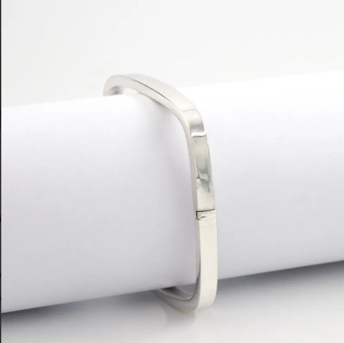 Pulsera cuadrada de plata sobre una superficie de mármol blanco con hojas de eucalipto cerca.